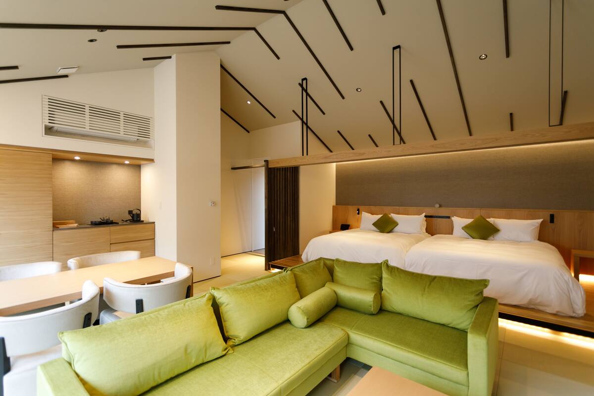 Una habitación de hotel moderna con un sofá verde, un cabecero de madera y una cama grande con ropa blanca.
