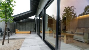 Une terrasse extérieure moderne, agrémentée d’un chemin en pierre, d’un espace salon et offrant une vue à travers de grandes portes vitrées.