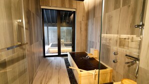Une salle de bain moderne dotée d’une douche à parois de verre, d’une baignoire en bois et d’un espace extérieur visible à travers la porte en verre.