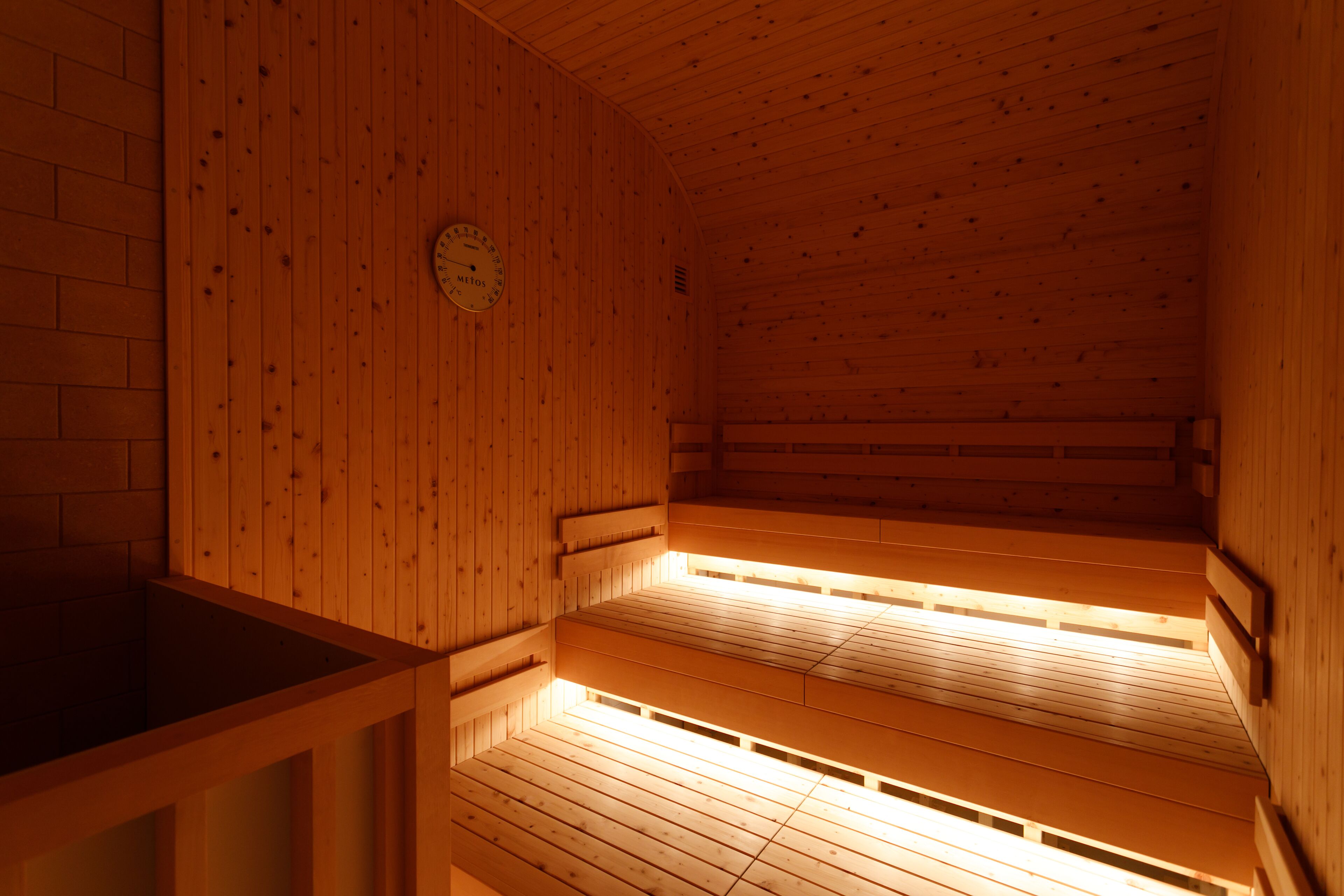 A sauna with wooden walls and benches, a visible clock, and a window for natural light.
