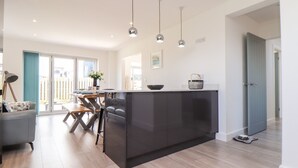 Une cuisine moderne dotée d’un îlot central, de luminaires suspendus et offrant une vue sur l’extérieur.