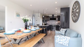 Une cuisine moderne avec des meubles de couleur sombre, un îlot central et un coin repas comprenant une table et des bancs en bois.