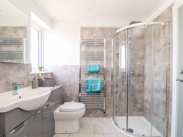 A modern bathroom with a glass-enclosed shower, a white toilet, and a vanity with a sink and mirror. - Amal Anpras (Tintagel)