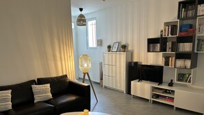 A modern living room with a black leather sofa, a white coffee table with candles, a white cabinet, a TV stand, and a bookshelf filled with books and DVDs. - Pleasant townhouse between Paris and Disneyland park (Vaires-sur-Marne)