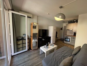 Ein kompakter Wohnbereich mit einer Couch, einem kleinen Esstisch, einer Küchenzeile und einer Glastür zum Balkon.