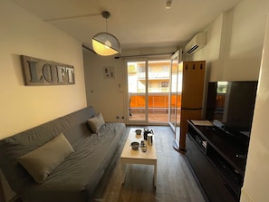 Ein Wohnzimmer mit Sofa, Couchtisch, Fernseher und einer Schiebetür, die auf einen Balkon im Freien führt.