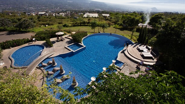 Ein Resort mit großem Schwimmbad, einer Brücke und Blick auf einen Berg.
