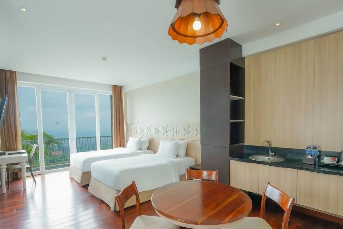 A hotel room with two beds, a dining table, and a kitchen area.