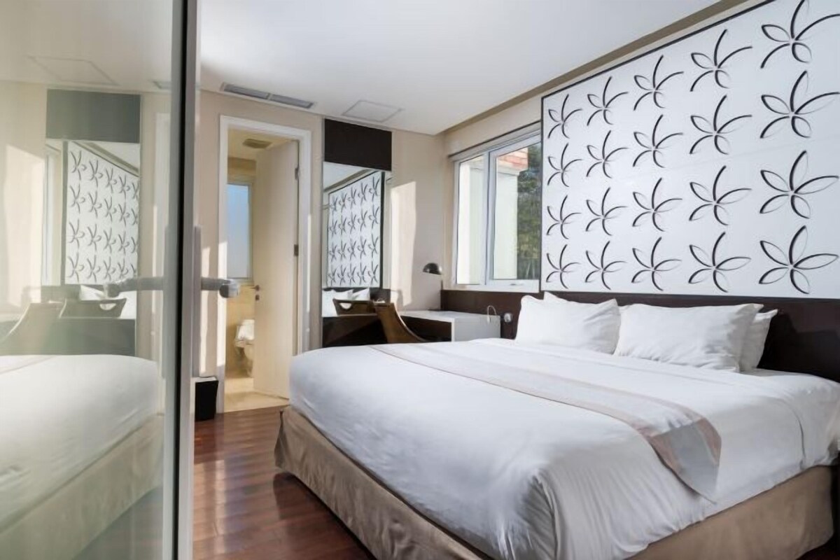 A bedroom with a bed, a desk, and a large window.