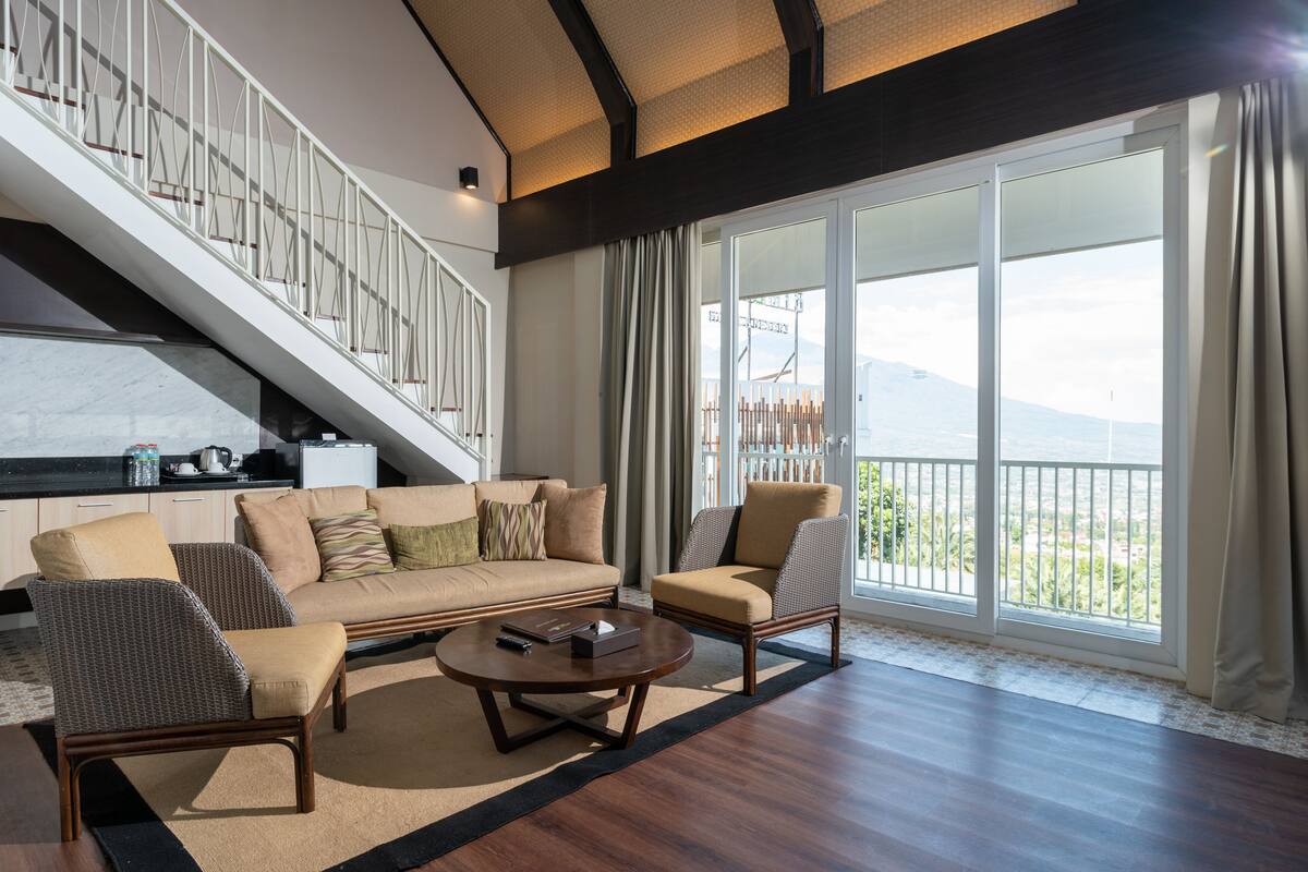 A spacious living area with a sofa, armchairs, a coffee table, and a staircase leading to an upper floor.