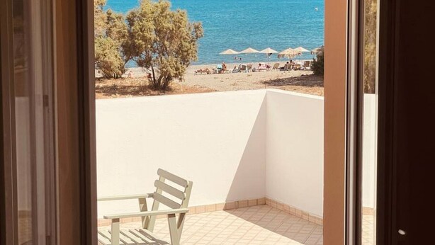 Ein Balkon mit freiem Blick auf das Meer, ein Strand mit Sonnenschirmen und einige Bäume.