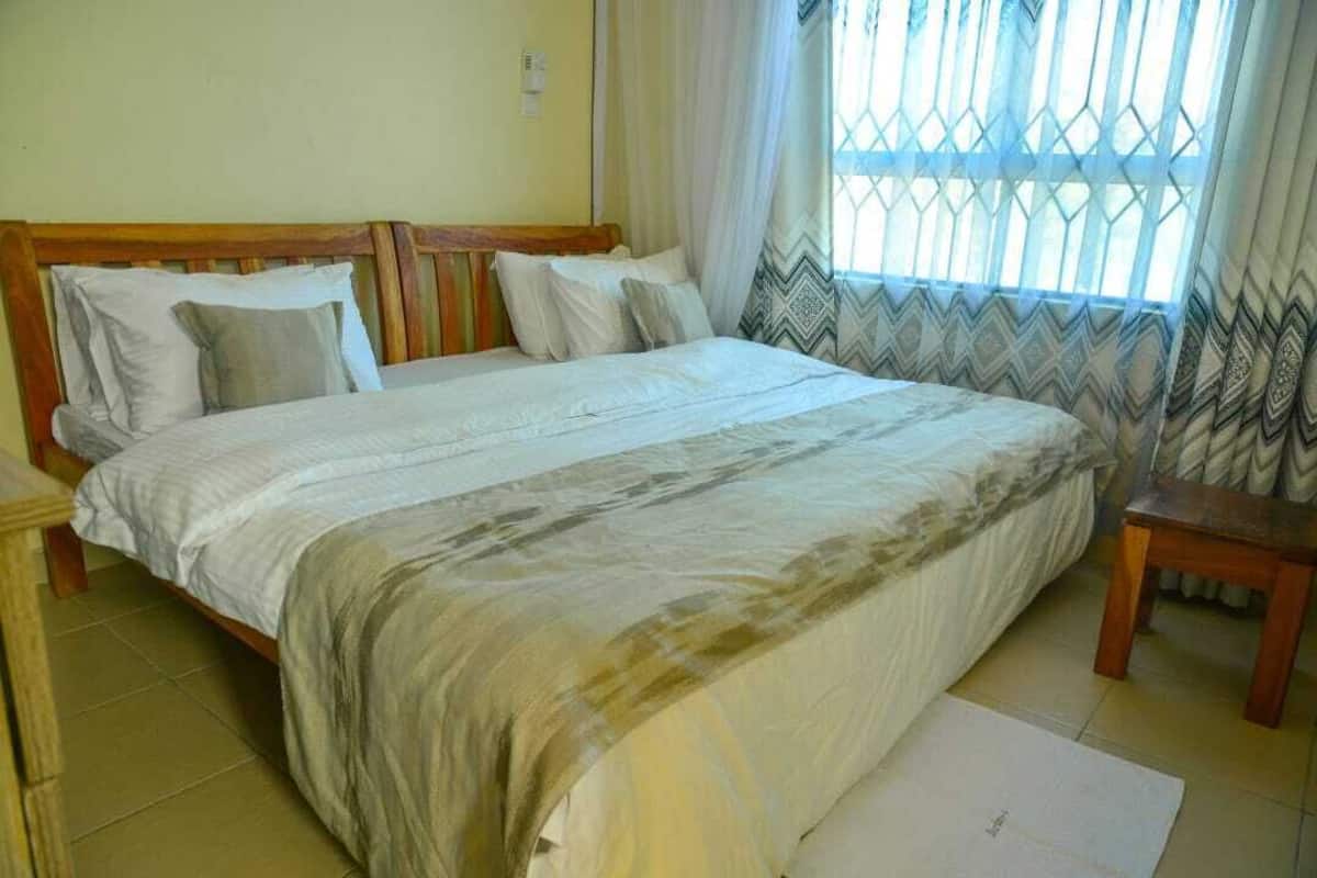 A double bed with a wooden headboard, a bedside table, and a window with patterned curtains.