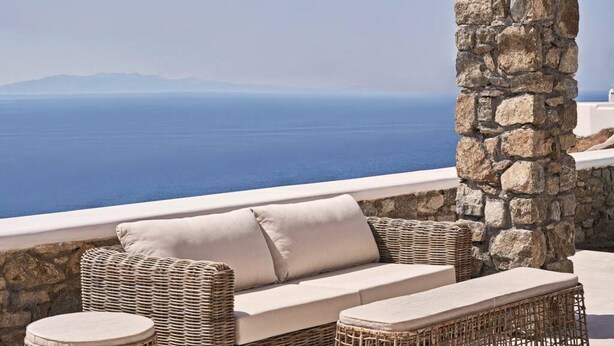 A wicker sofa with cushions, a round table, and a stone pillar in a seaside setting. - Villa Licata - 2BD, Luxury villa, near beach Elia (Elia)