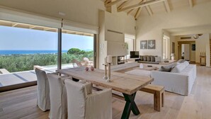 Un'ampia zona giorno con un tavolo da pranzo in legno, posti a sedere confortevoli, una televisione e vista sul mare.