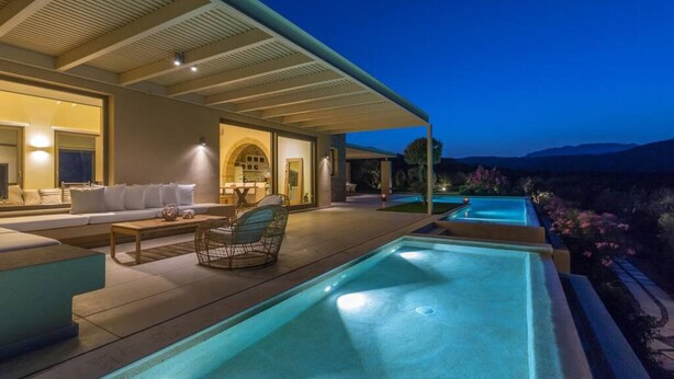 Una casa moderna con una grande piscina esterna, un patio coperto e vista sulle montagne.