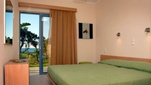 Ein Schlafzimmer mit einem Bett, einem Holztisch, einem grünen Stuhl und Blick ins Freie.