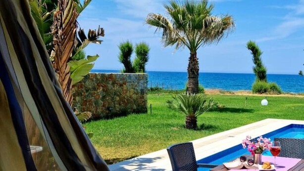 Ein Poolbereich mit Tisch und Stühlen, einer Steinmauer und Blick auf das Meer.