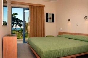 A bedroom with a bed, a wooden desk, a green chair, and a view of the outdoors.