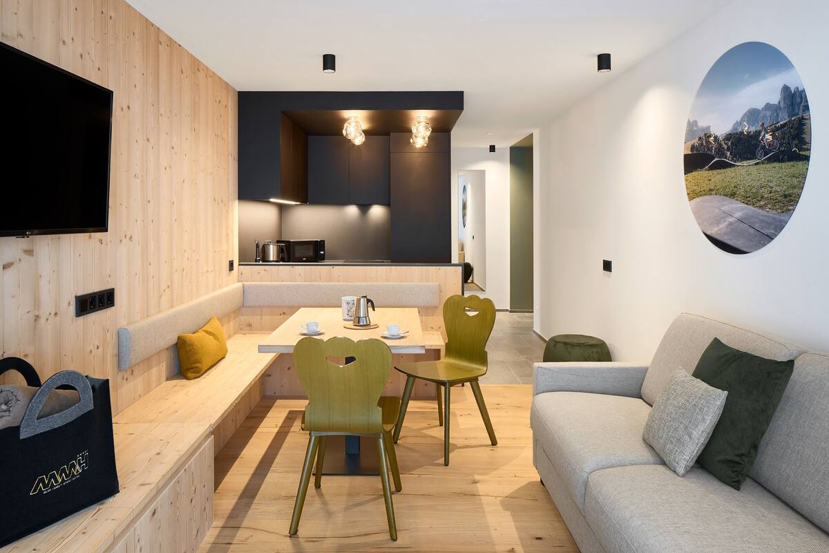 A modern living room with a sofa, two chairs, a dining table, and a TV mounted on the wall.