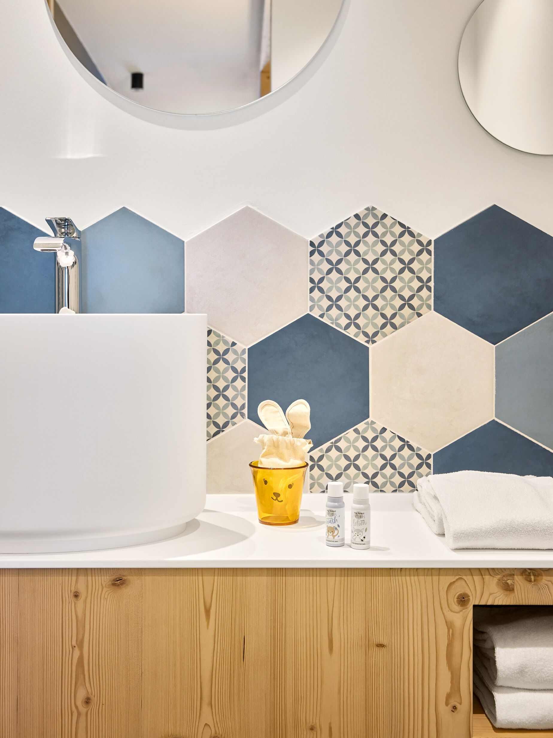 A bathroom with a white sink, a mirror, a wooden vanity, and a patterned hexagonal tile backsplash.