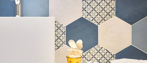 A bathroom with a white sink, a mirror, a wooden vanity, and a patterned hexagonal tile backsplash.