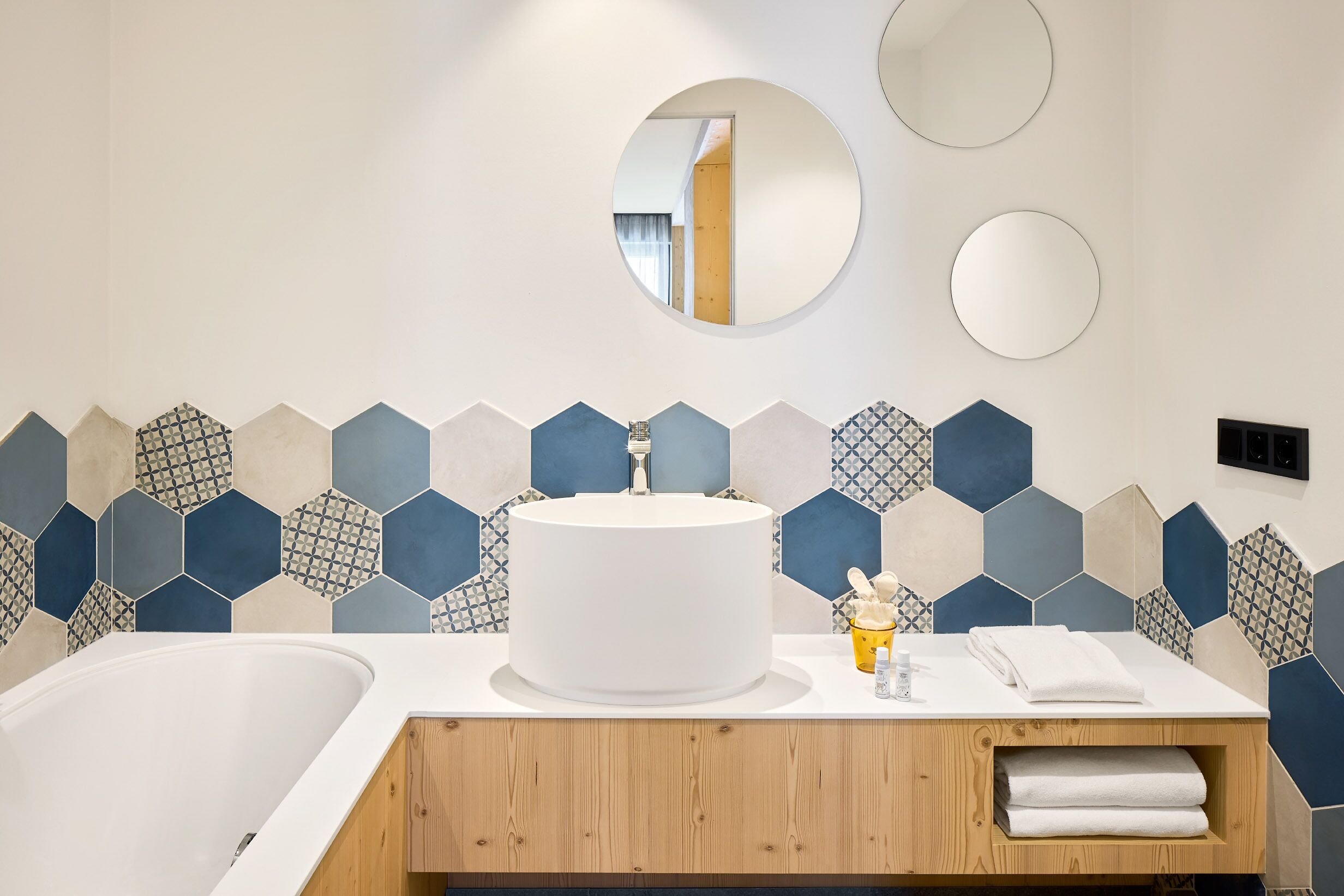 A modern bathroom with a white sink, a large mirror, and a hexagonal tile backsplash.