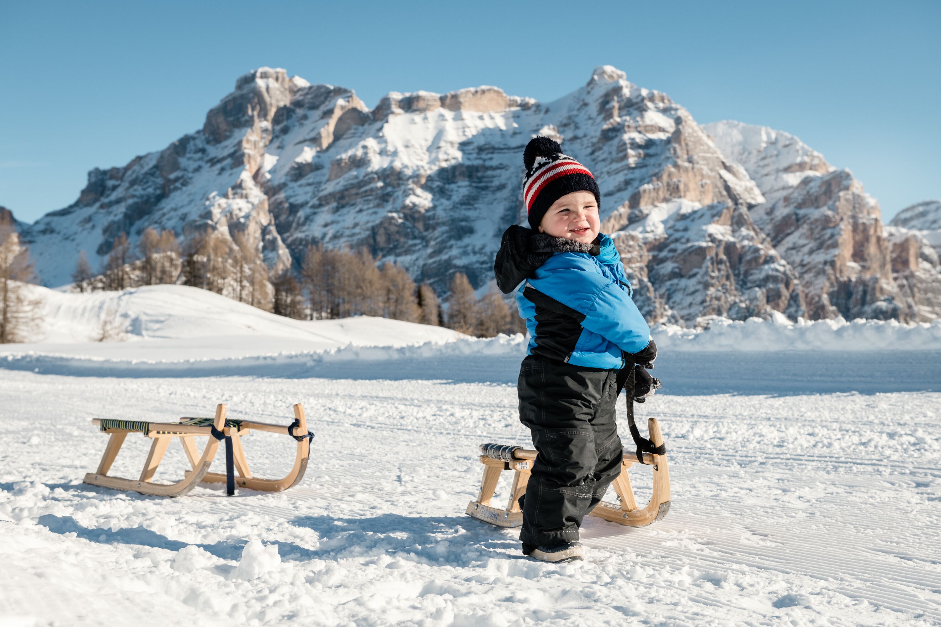 A child sledding on a snowy slope with a mountainous backdrop.
