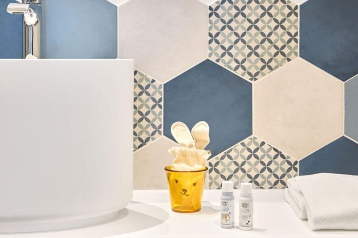 A bathroom with a white bathtub, a yellow cup with a bunny design, and two bottles of lotion.