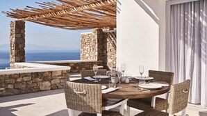 An outdoor dining area with a stone wall, wicker chairs, and a wooden table set for two. - Villa Bellagio - 1BD Luxury villa, near beach Elia (Elia)