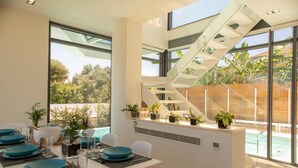 Un comedor moderno con escalera de cristal, ventanas amplias y plantas en macetas.
