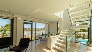 Un interior moderno con zona de comedor, escalera y ventanas amplias.