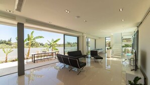 Amplia sala de estar moderna con ventanas grandes, un espacio de descanso con sofá y sillones, y una escalera que sube a un nivel superior.