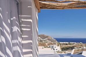 A white building with a view of a coastal landscape, including a mountain and the sea.