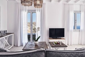 A modern living room with a sofa, a coffee table with a plant, a flat-screen TV, and a view of the sea through large windows.