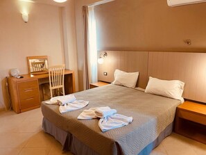 Hotellihuone, jossa on suuri sänky, puinen työpöytä, tuoli ja yöpöytä.