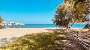 Una platja amb una tanca de fusta, una zona verda i ombrelles al fons.