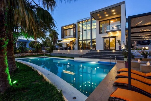 A modern two-story house with a swimming pool, outdoor seating, and a well-lit entrance.