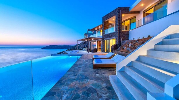A modern building with a swimming pool, outdoor seating, and a view of the sea. - Villa Blue Lagoon -Unifying your luxury senses -SEAFRONT (Chania Akrotiri)