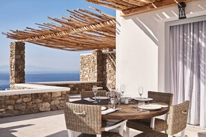 An outdoor dining area with a stone wall, wicker chairs, and a wooden table set for two.