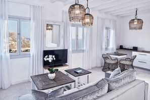 Un salon moderne comprenant un canapé, un téléviseur, des fauteuils en osier et un coin repas avec une table et des chaises.