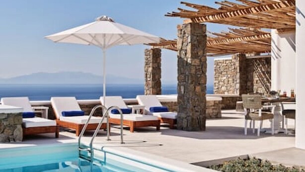 A pool area with lounge chairs and umbrellas, stone pillars, and a view of the sea. - Villa Vassena - 1BD, Luxury villa, near beach Elia (C9HP+7QR Mikonos, Greece)