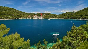 Vista sulla costa con acque turchesi cristalline, una piccola barca ancorata vicino alla riva e un gruppo di edifici su un pendio.