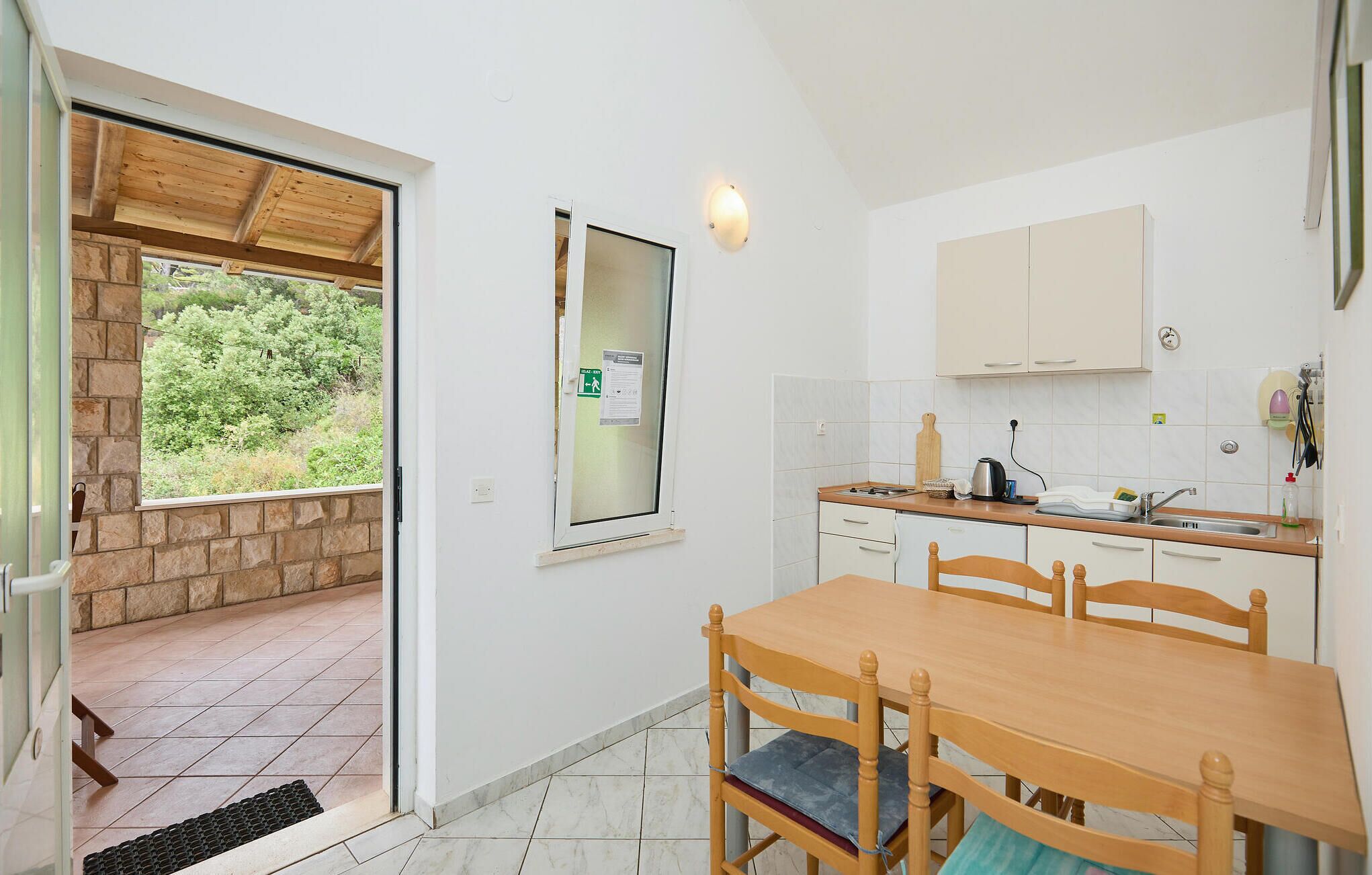 A compact kitchen with a wooden table and chairs, a built-in oven, and a view of greenery outside.