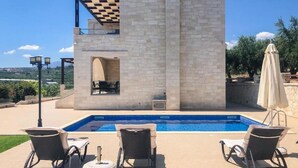 Un espace aménagé au bord de la piscine, avec un bâtiment en pierre, des sièges extérieurs et une vue sur le paysage.