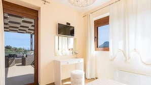 Une chambre à coucher avec un grand lit, une commode blanche, un miroir, une télévision et une vue sur l’extérieur.