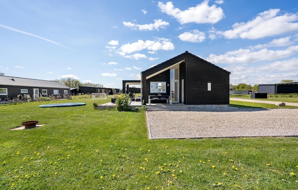 Een modern gebouw met een donkere gevel, een overdekt terras en een verzorgd gazon met een zwembadje en tuin.