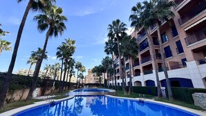 A pool area with palm trees and a multi-story building in the background. - Vilamar-1-d  VYB Sea Views (Denia)
