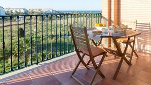 A balcony with a table set for two, a chair, and a view of the sea and greenery. - Vilamar-1-d  VYB Sea Views (Denia)