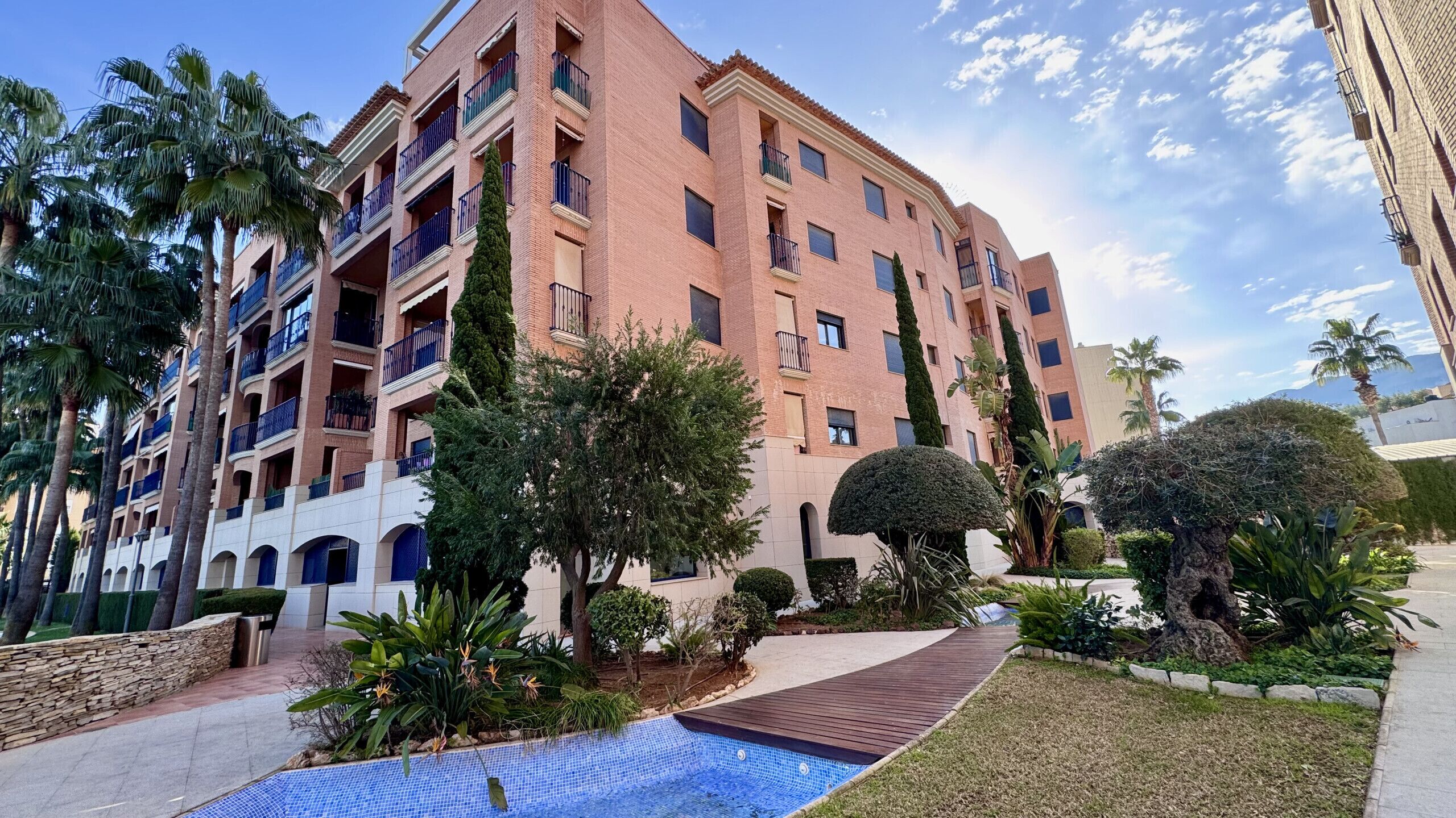Un edificio residencial de varios pisos con balcones, piscina y jardines ajardinados.