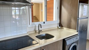 Une cuisine moderne dotée d’une hotte en acier inoxydable, d’un lave-vaisselle encastré, d’une machine à laver et d’une fenêtre donnant sur un escalier.